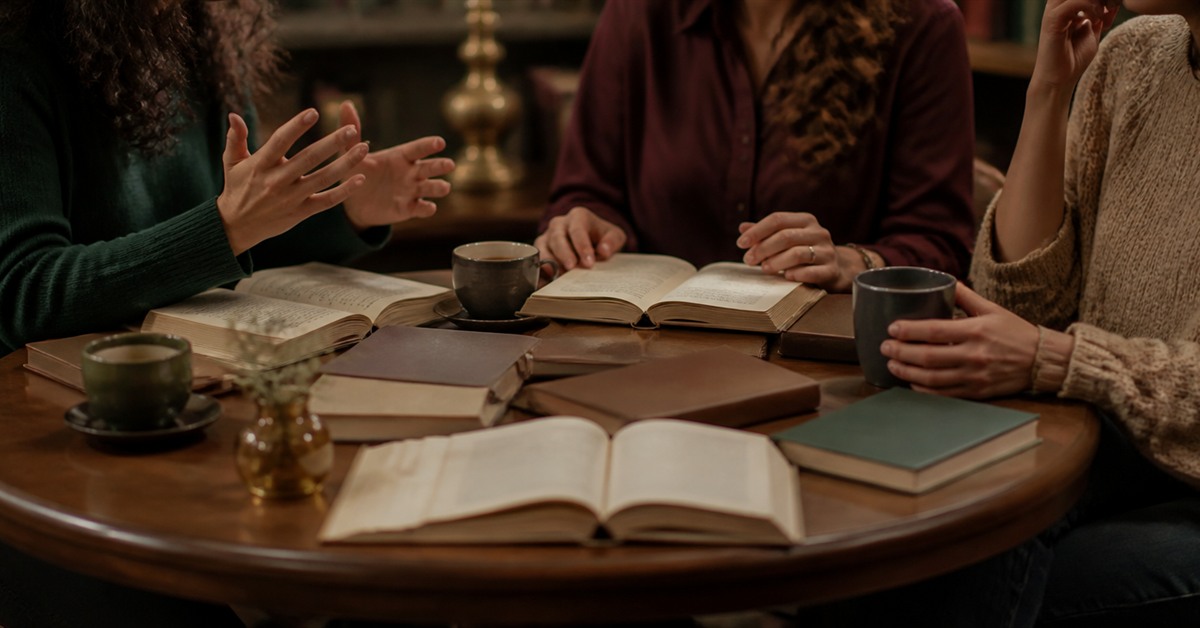 Bir kafe masasında aralarında açık kitaplar bulunan üç arkadaşın rahat bir kitap sohbeti